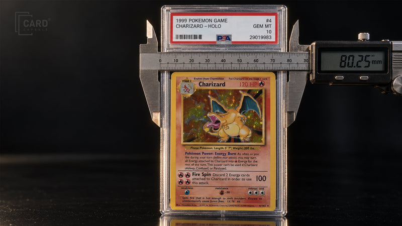 Digital caliper measuring the 80.25 mm width of a standard PSA slab, shown on a PSA 10 1999 Pokemon Charizard holo