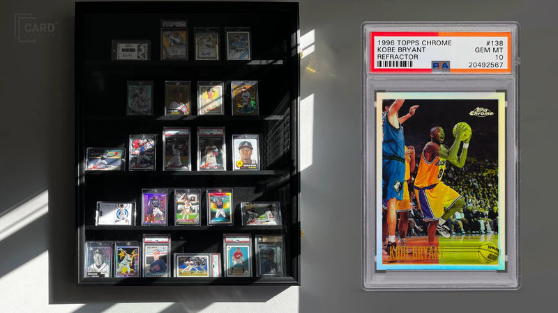 Graded cards displayed on a wall with direct sunlight falling across them, beside a PSA-graded slab