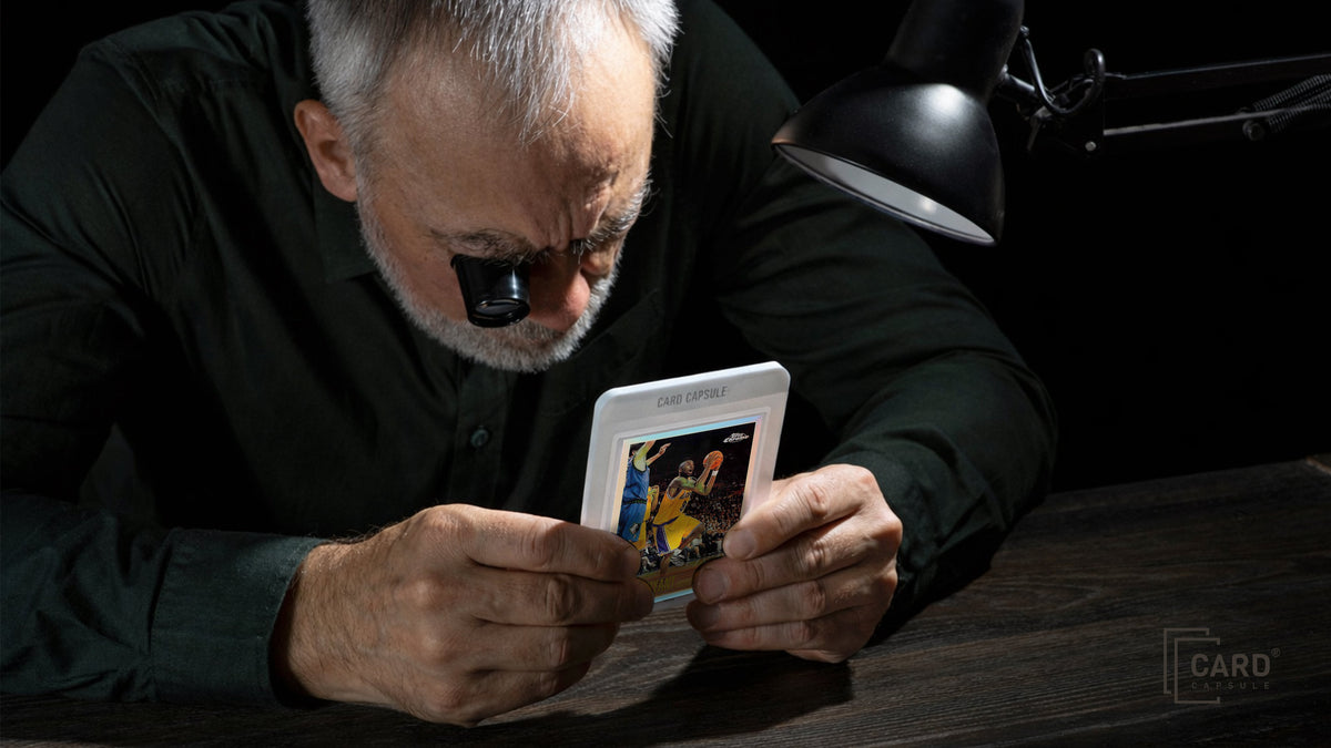 Collector examining a sports card with a jeweler's loupe under a desk lamp